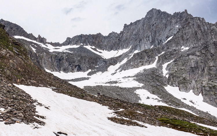 Wanderer überqueren ein Schneefeld in einem felsigen Alpenkar