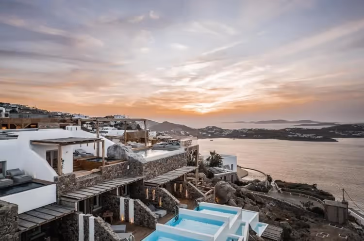 Witte terrassen met zwembaden boven de zee in Mykonos bij zonsondergang