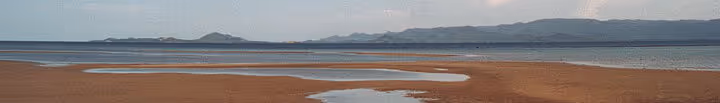 Panorama av sandstrand med vann og fjell i det fjerne