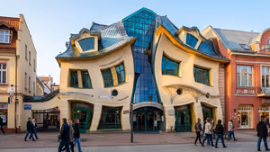 Casa Storta di Sopot con pareti color crema deformate, tetto ondulato e finestre verdi ricurve, con pedoni di passaggio