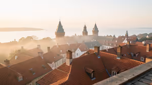 Rote Ziegeldächer und mittelalterliche Türme der Altstadt von Tallinn im Morgennebel, dahinter die Ostsee