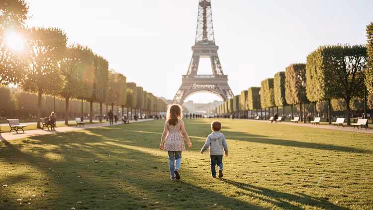Zwei kleine Kinder laufen bei tief stehender Sonne über den Rasen des Marsfelds auf den Eiffelturm in Paris zu