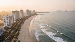Luftaufnahme eines langen Sandstrands mit Palmen und Hotelhochhäusern in Pattaya, Wellen rollen bei Sonnenuntergang an