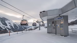 Illustration: Gondelkabinen verlassen eine leere verschneite Liftstation mit geschlossenem Kassenhäuschen, dahinter bewaldete Hänge