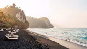 Schwarzer Sandstrand auf Bali mit Liegenreihen, Palmen und einem kleinen Schrein auf einer Klippe über dem Meer