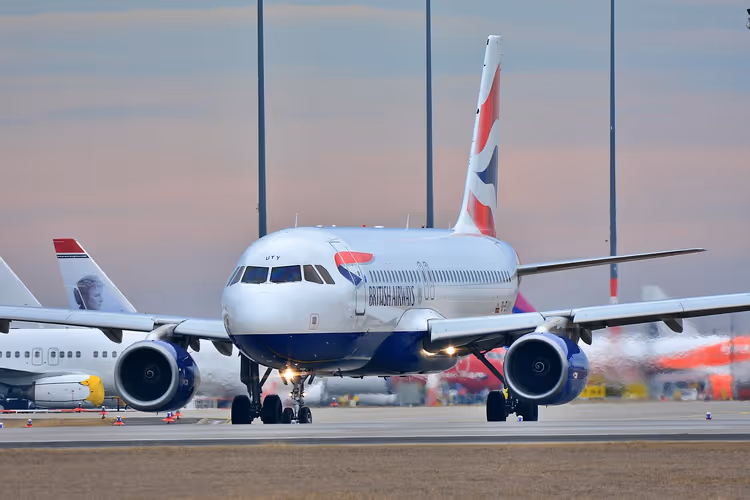 Passagierjet rollt in der Dämmerung frontal über das Flughafenvorfeld, dahinter die Leitwerke anderer Flugzeuge