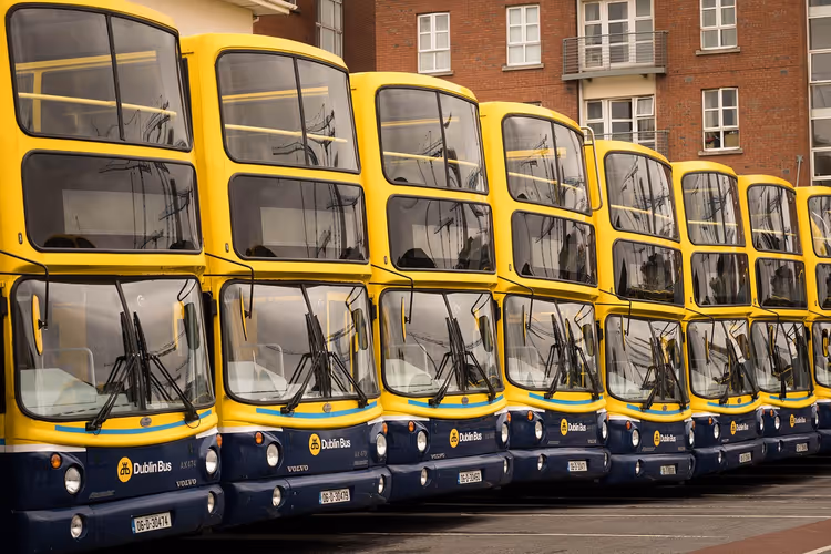 Reihe gelb-blauer Doppeldeckerbusse von Dublin Bus, nebeneinander geparkt vor einem Backsteingebäude