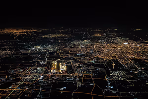 Nächtliche Luftaufnahme einer weitläufigen Stadt mit einem Raster aus orangefarbenen und weißen Straßenlichtern bis zum Horizont