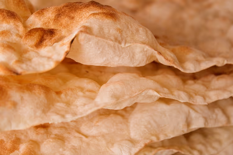 Primo piano di sottili sfoglie di pane lavash impilate, con bolle dorate e brunite