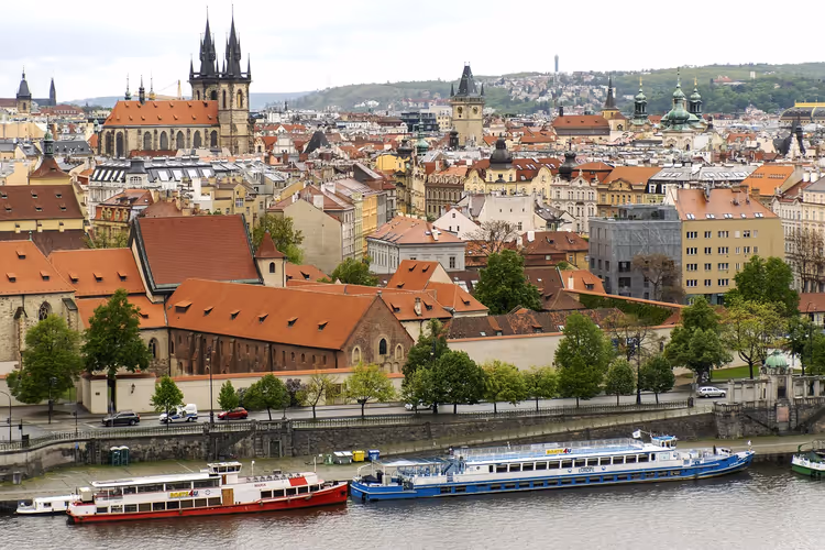 Rote Dächer und gotische Kirchtürme der Prager Altstadt über der Moldau, am Kai liegen Ausflugsschiffe