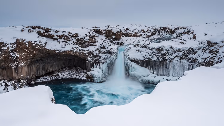 Aldeyjarfoss-Wasserfall im Winter zwischen schneebedeckten Felswänden in Island