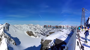 Skifahrer und Besucher auf einer Aussichtsplattform über verschneiten Alpengipfeln unter tiefblauem Himmel in Österreich