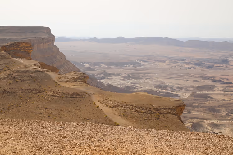 Karge Wüstenklippen und eine weite, felsige Kraterebene, die sich bis zu dunstigen Hügeln erstreckt, Israel