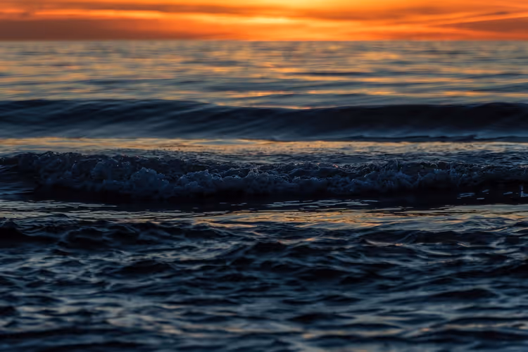 havbølger ved solnedgang under en oransje himmel