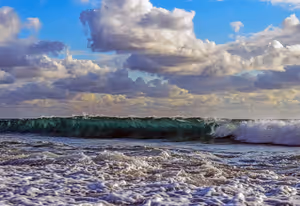 Grüne Welle bricht am Ufer zu weißem Schaum unter blauem Himmel mit schweren Wolken, als Sinnbild für das Meer bei Ayia Napa