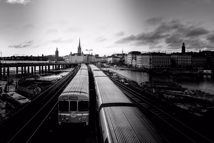 Schwarz-Weiß-Blick auf U-Bahn-Züge auf Gleisen in Richtung Stockholmer Altstadt mit Kirchtürmen jenseits des Wassers