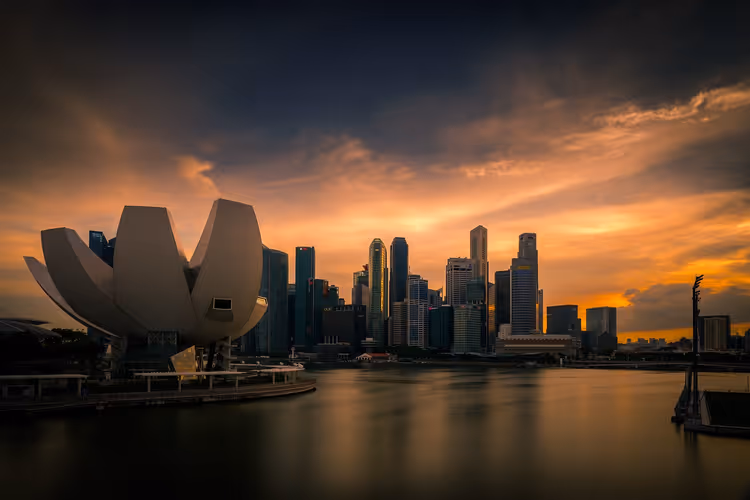 Museumsbau in Lotusform und Wolkenkratzer von Singapur jenseits der Bucht unter orangefarbenem Abendhimmel mit dunklen Wolken