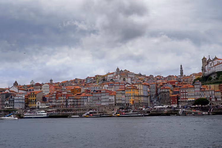 Uferviertel Ribeira in Porto mit bunten, übereinander gestaffelten Häusern und Ausflugsbooten auf dem Douro unter schweren grauen Wolken
