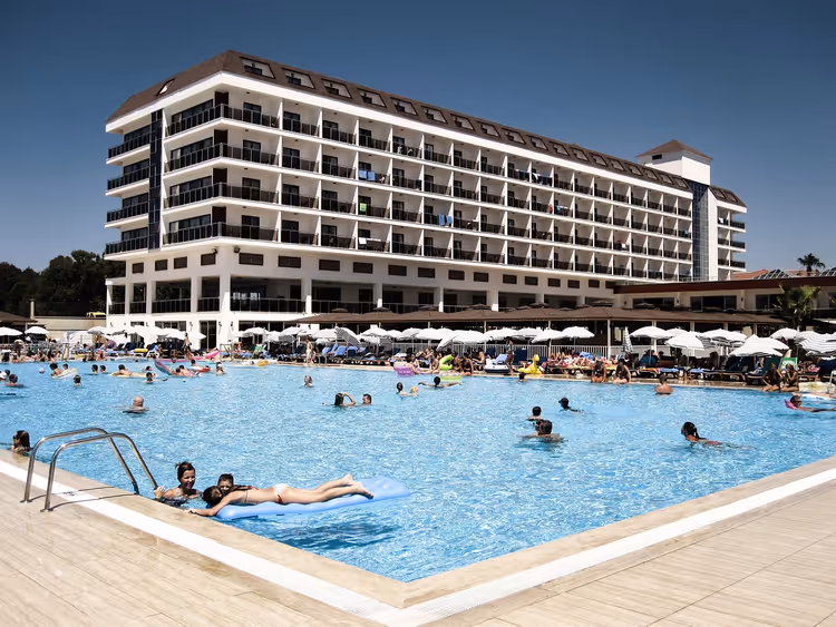 Groot wit hotel met een zwembad en ligstoelen