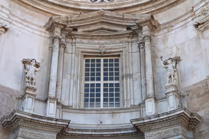 Barocke Steinfassade mit großem Sprossenfenster, eingerahmt von Säulen und zwei Statuen auf Sockeln, Cádiz
