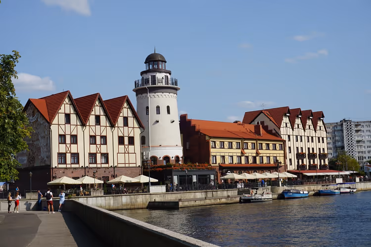 Fachwerkhäuser und ein weißer Leuchtturm an der Uferpromenade am Fluss in Kaliningrad an einem sonnigen Tag