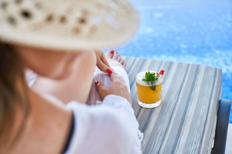 vrouw met hoed en cocktail bij het zwembad