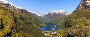 Geirangerfjord von oben mit Kreuzfahrtschiffen auf blauem Wasser zwischen grünen Hängen und schneebedeckten Gipfeln