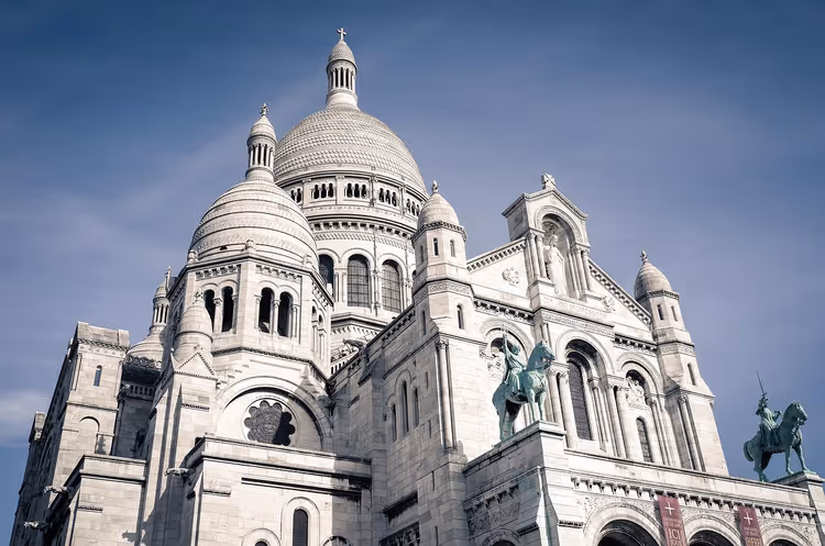 Weiße Kuppeln und Türmchen der Basilika Sacré-Cœur in Paris von unten gesehen, mit grünen Reiterstatuen