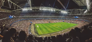 Voll besetztes Fußballstadion bei Nacht vom Oberrang aus, Flutlicht fällt während eines Spiels auf den grünen Rasen