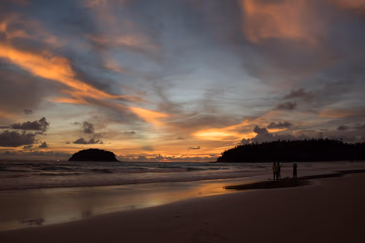 Solnedgang på Kata Beach med silhuetter av mennesker