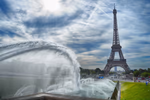 Eiffelturm in Paris von den Trocadéro-Brunnen aus gesehen, mit Wasserbögen unter bewölktem Himmel
