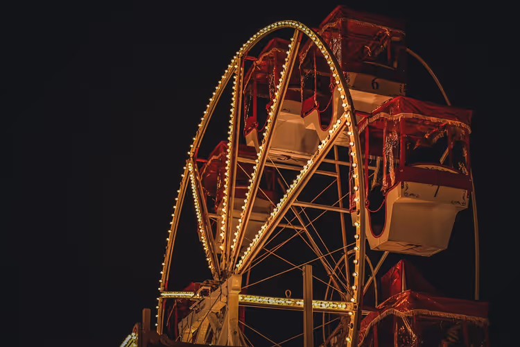 Riesenrad mit roten Gondeln und Felgen, die von warmen Glühbirnen nachgezeichnet sind, vor schwarzem Nachthimmel