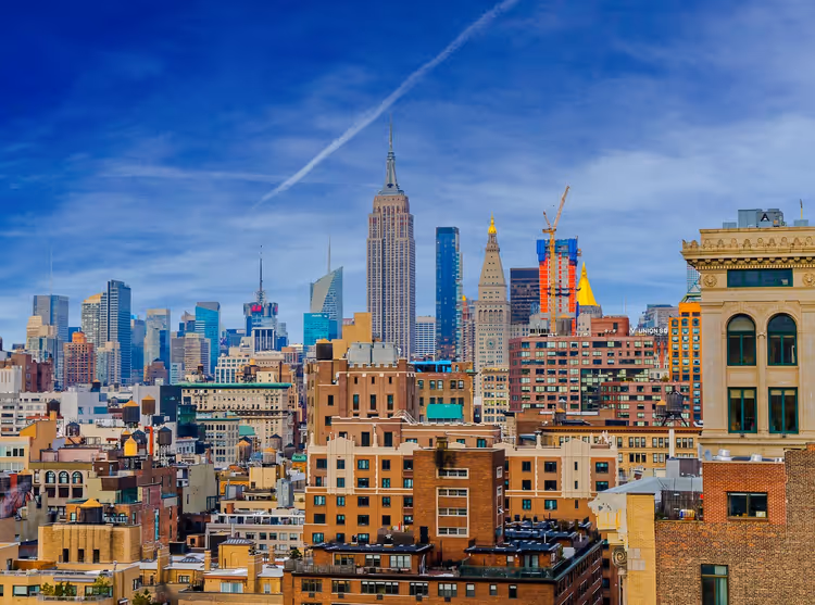 أفق مانهاتن ومبنى إمباير ستيت يرتفع فوق عمارات سكنية من الطوب تحت سماء زرقاء في نيويورك