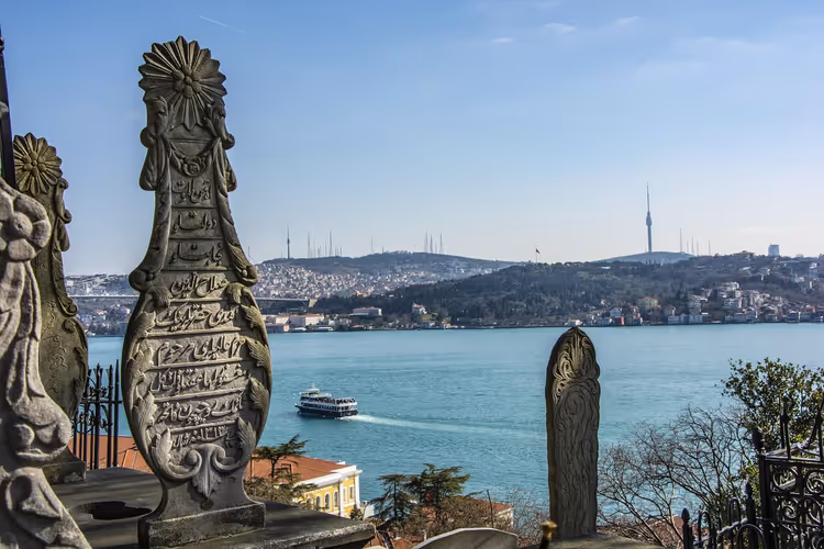 Verzierte osmanische Grabsteine an einem Hang über dem Bosporus in Istanbul, eine Fähre überquert das blaue Wasser
