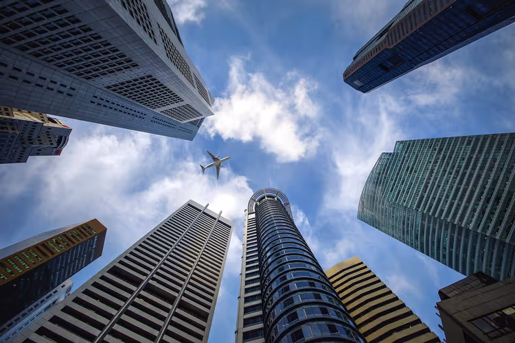Blick von unten auf Wolkenkratzer in Singapur, die zum bewölkten blauen Himmel zusammenlaufen, darüber ein Flugzeug
