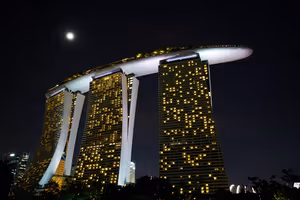 Drei beleuchtete Hoteltürme, verbunden durch eine schiffsförmige Dachterrasse, nachts bei Vollmond in Singapur