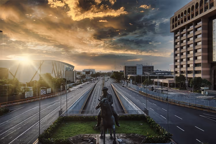 Reiterstandbild auf einer begrünten Verkehrsinsel zwischen leeren Stadtautobahnen bei Sonnenuntergang unter dramatischen Wolken