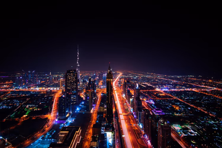 Skyline von Dubai bei Nacht von oben, mit beleuchteten Autobahnen, Wolkenkratzern und der Spitze des Burj Khalifa in der Ferne