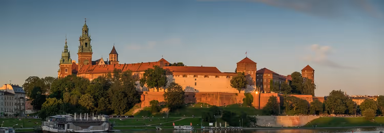 Complesso di un castello con mura in mattoni rossi, torri e la guglia di una cattedrale su un colle boscoso sopra un fiume in Polonia