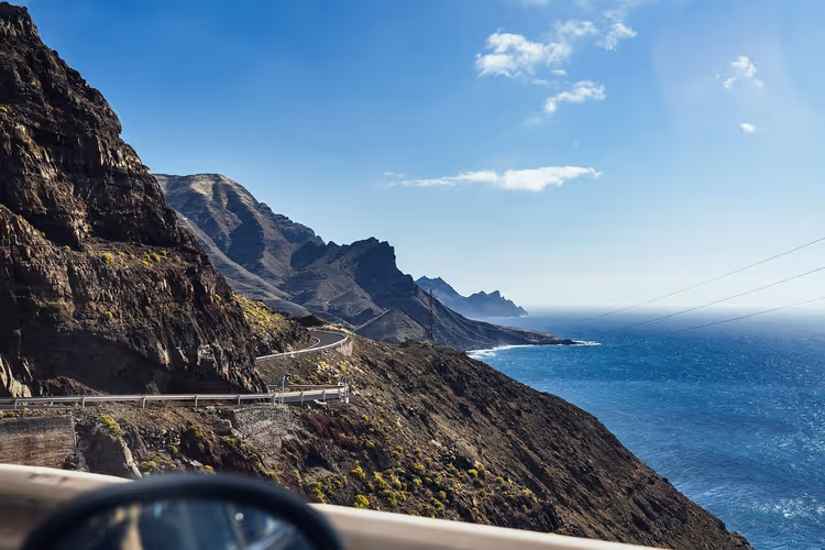 Kurvige Küstenstraße in dunklen Vulkanklippen über dem blauen Atlantik auf den Kanarischen Inseln, Blick aus dem Auto
