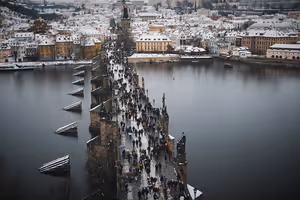 Menschenmengen gehen über die Karlsbrücke über die Moldau in Prag, am anderen Ufer schneebedeckte Dächer