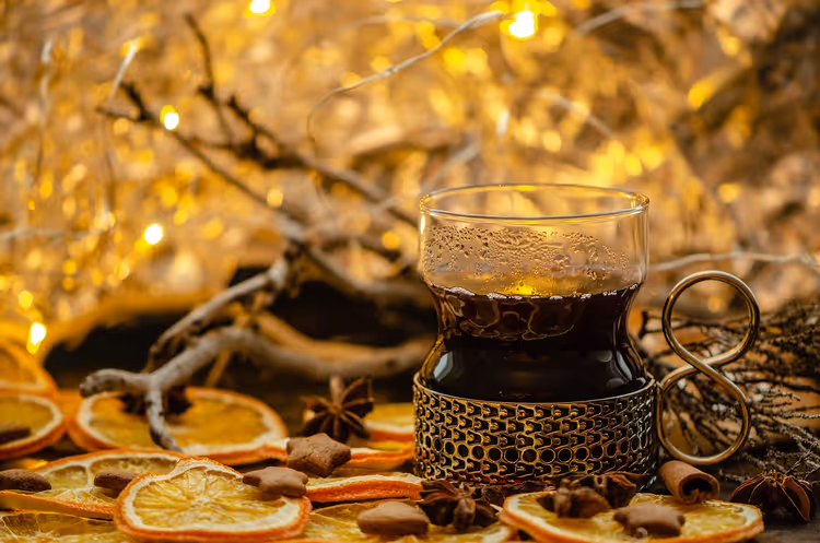 Glas Glühwein in einem Metallhalter zwischen getrockneten Orangenscheiben, Sternanis und warmen Lichterketten