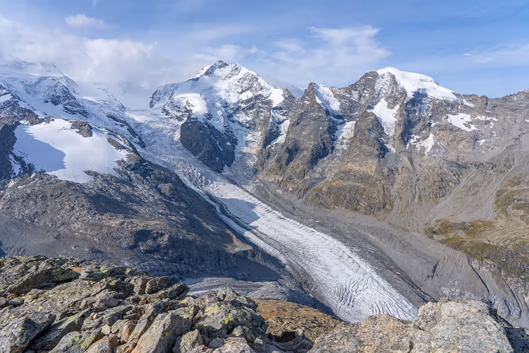 Alpengletscher windet sich zwischen schneebedeckten Gipfeln talwärts, von einem Felsgrat in der Berninagruppe gesehen