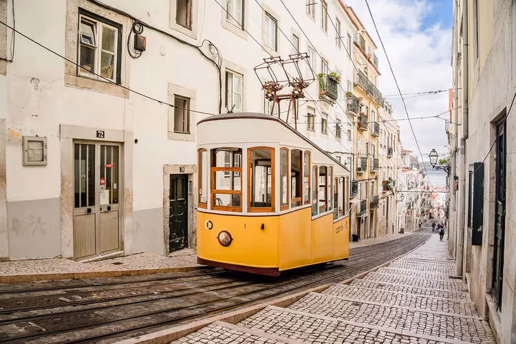 Gelbe historische Standseilbahn fährt eine steile Kopfsteinpflastergasse zwischen hellen alten Häusern hinauf