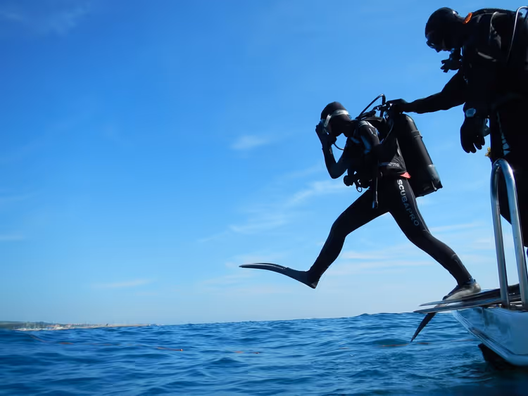 Dykker som hopper fra en båt ned i det blå havet