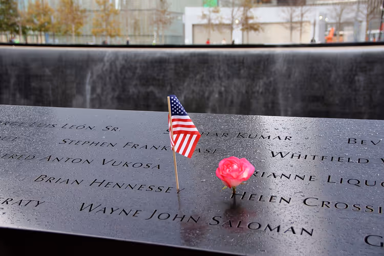 имена на мемориале 9/11 с флажком и розой