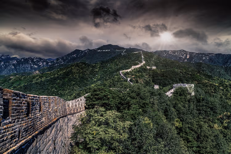 Chinesische Mauer windet sich über bewaldete grüne Bergkämme unter dunklen Gewitterwolken