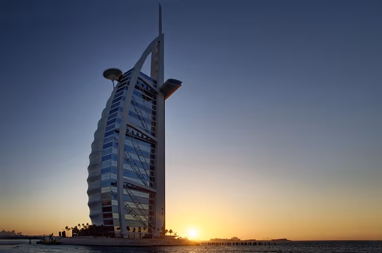 Segelförmiges Hotel Burj Al Arab in Dubai als Silhouette vor dem Himmel bei Sonnenuntergang über dem Meer