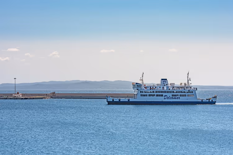 Hvit Delcomar-ferge som seiler forbi en molo på havet