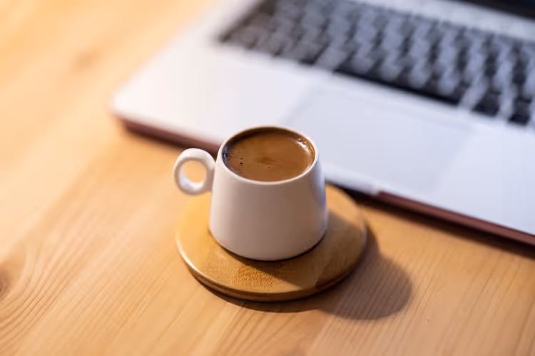 Kopp kaffe på ett bord framför en laptop